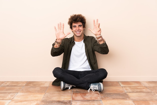 Giovane uomo caucasico che si siede sul pavimento che conta nove con le dita