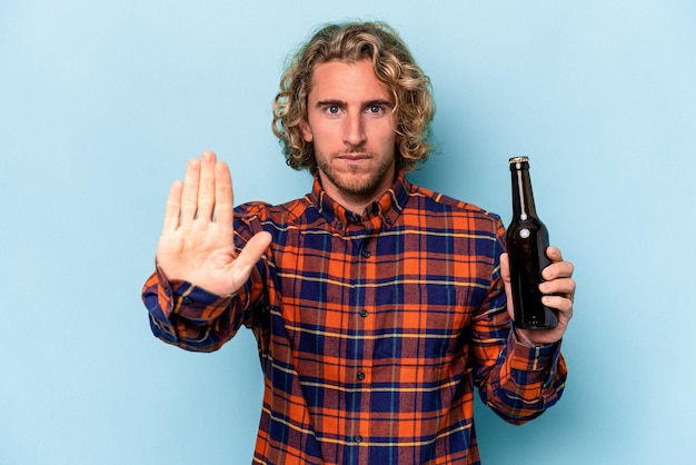 Giovane uomo caucasico che tiene birra isolata su sfondo bianco in piedi con la mano tesa che mostra il segnale di stop, impedendoti.