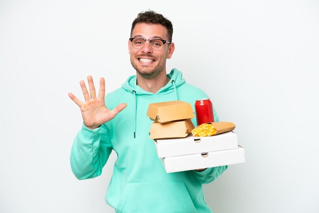 Giovane uomo caucasico che tiene fast food isolato su sfondo bianco contando cinque con le dita