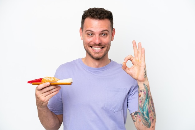 Giovane uomo caucasico che tiene il sashimi isolato su sfondo bianco che mostra il segno ok con le dita