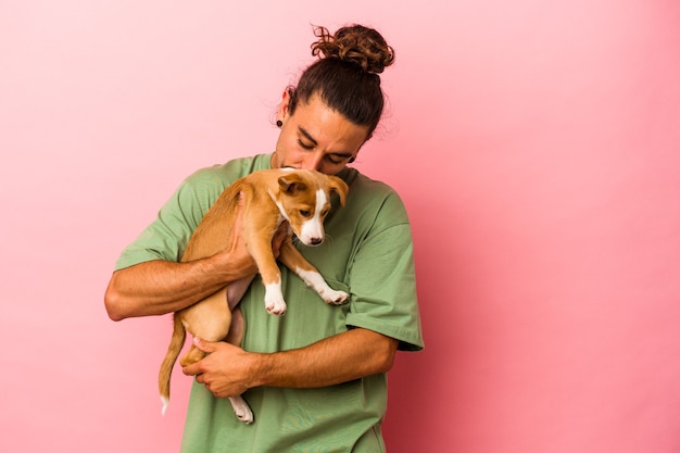 Giovane uomo caucasico che tiene il suo cucciolo isolato su sfondo rosa