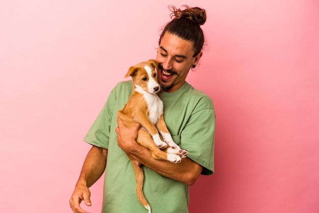 Giovane uomo caucasico che tiene il suo cucciolo isolato su sfondo rosa