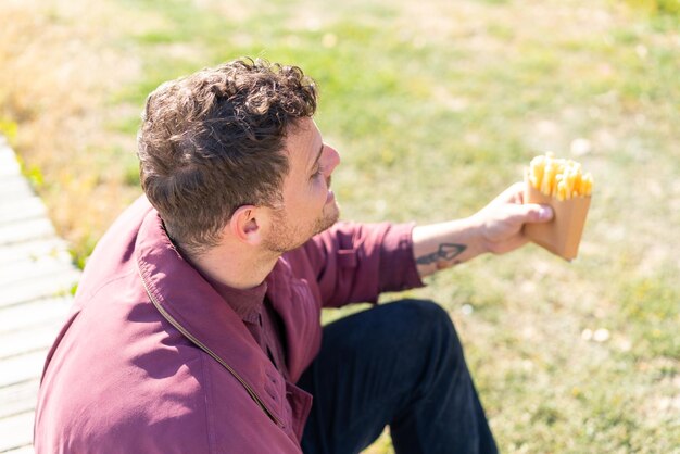 Giovane uomo caucasico che tiene patatine fritte all'aperto con felice espressione