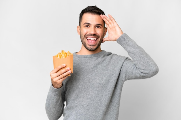 Giovane uomo caucasico che tiene patatine fritte su sfondo bianco isolato con espressione sorpresa