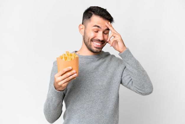 Giovane uomo caucasico che tiene patatine fritte su sfondo bianco isolato ridendo