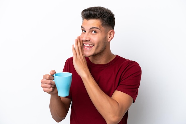 Giovane uomo caucasico che tiene tazza di caffè isolato su sfondo bianco sussurrando qualcosa