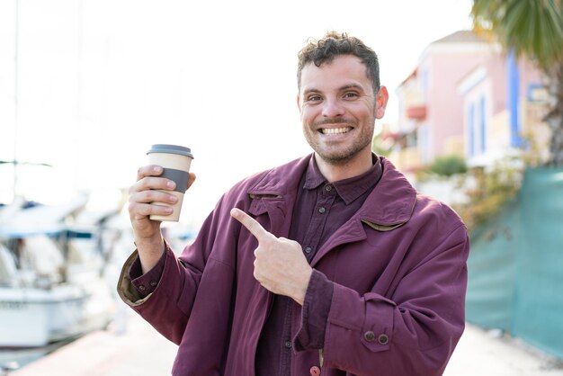 Giovane uomo caucasico che tiene un caffè da asporto all'aperto e lo indica