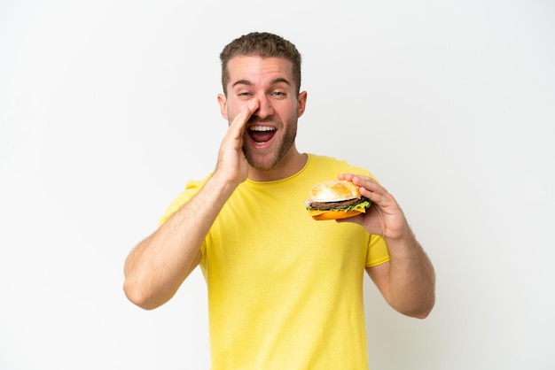 Giovane uomo caucasico che tiene un hamburger isolato su sfondo bianco gridando con la bocca spalancata