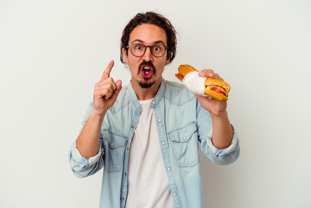 Giovane uomo caucasico che tiene un panino isolato su bianco avendo un'idea, concetto di ispirazione.