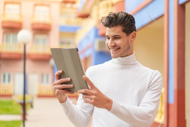 Giovane uomo caucasico che tiene un tablet all'aperto con felice espressione