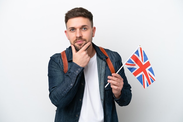 Giovane uomo caucasico che tiene una bandiera del Regno Unito isolata su sfondo bianco pensando
