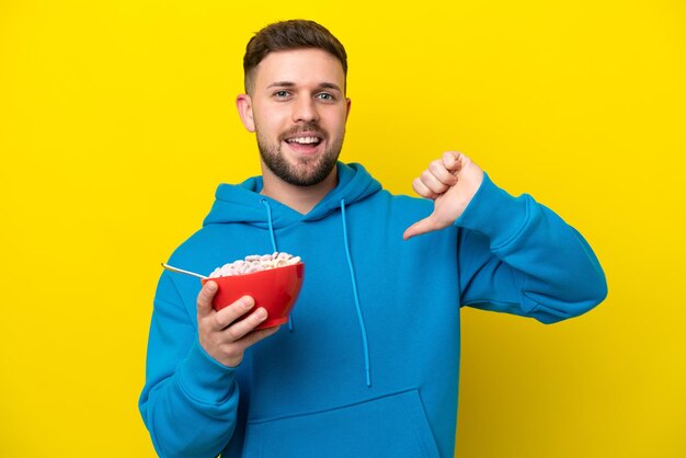 Giovane uomo caucasico che tiene una ciotola di cereali isolata su sfondo giallo orgoglioso e soddisfatto di sé