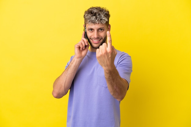 Giovane uomo caucasico che usa il telefono cellulare isolato su sfondo giallo facendo un gesto imminente