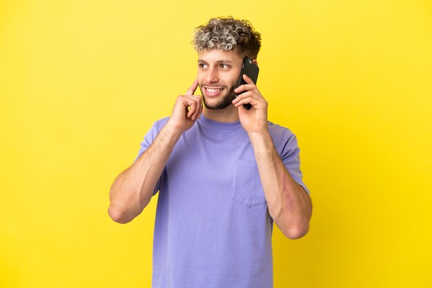 Giovane uomo caucasico che utilizza il telefono cellulare isolato su sfondo giallo pensando a un'idea mentre guarda in alto