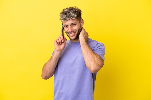 Giovane uomo caucasico che utilizza il telefono cellulare isolato su sfondo giallo ridendo