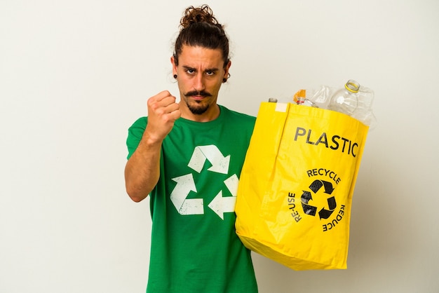 Giovane uomo caucasico con capelli lunghi che riciclano plastica isolata su fondo bianco che mostra pugno alla telecamera, espressione facciale aggressiva.