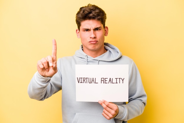 Giovane uomo caucasico con cartello virtuale isolato su sfondo giallo che mostra il numero uno con il dito