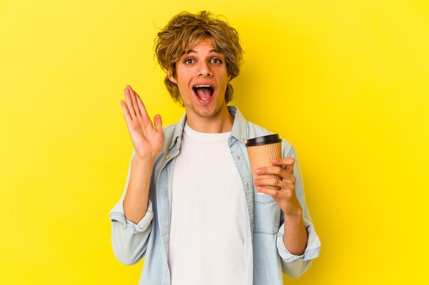Giovane uomo caucasico con il trucco in possesso di un caffè da asporto isolato su sfondo giallo sorpreso e scioccato.
