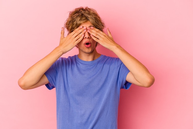 Giovane uomo caucasico con make up isolato su sfondo rosa impaurito che copre gli occhi con le mani.