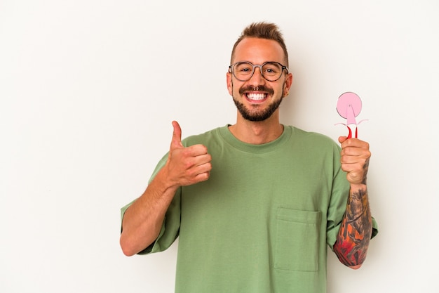 Giovane uomo caucasico con tatuaggi che tengono lecca-lecca isolato su sfondo bianco sorridente e alzando il pollice