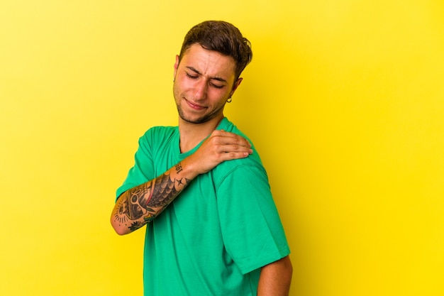 Giovane uomo caucasico con tatuaggi isolati su sfondo giallo con dolore alla spalla.