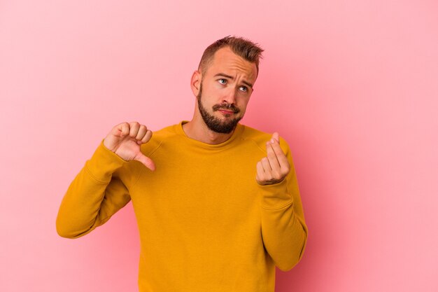 Giovane uomo caucasico con tatuaggi isolati su sfondo rosa che mostra che non ha soldi.