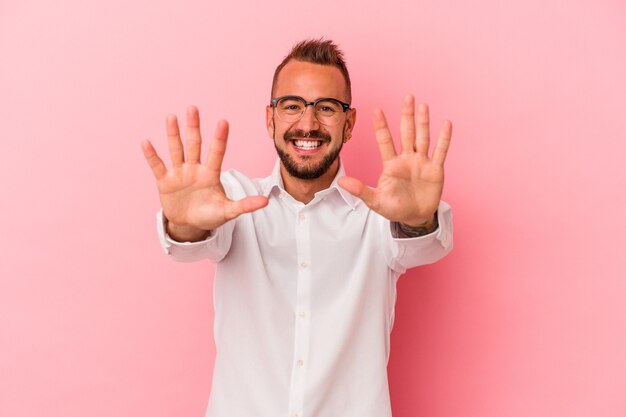 Giovane uomo caucasico con tatuaggi isolati su sfondo rosa che mostra il numero dieci con le mani.