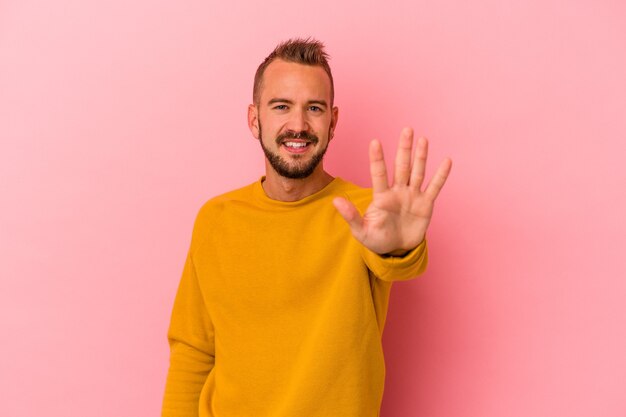 Giovane uomo caucasico con tatuaggi isolati su sfondo rosa sorridente allegro che mostra il numero cinque con le dita.