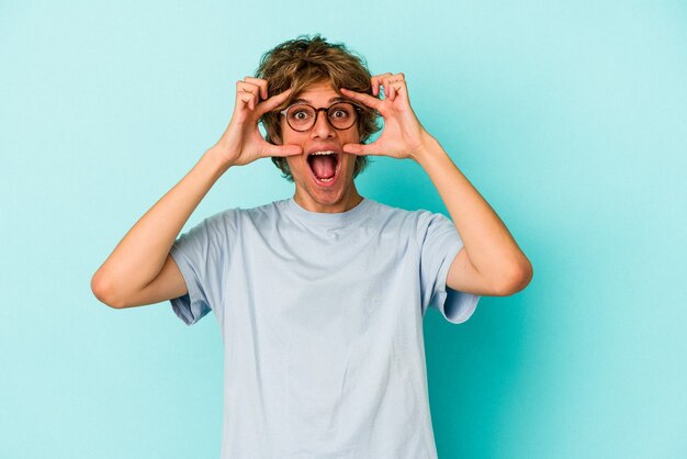 Giovane uomo caucasico con trucco isolato su sfondo blu tenendo gli occhi aperti per trovare un'opportunità di successo.