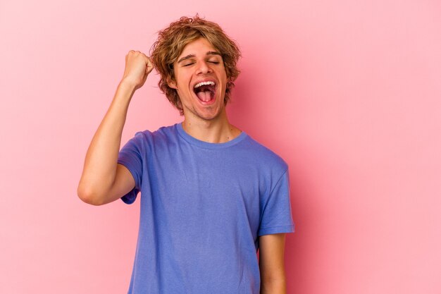 Giovane uomo caucasico con trucco isolato su sfondo rosa che celebra una vittoria, passione ed entusiasmo, espressione felice.