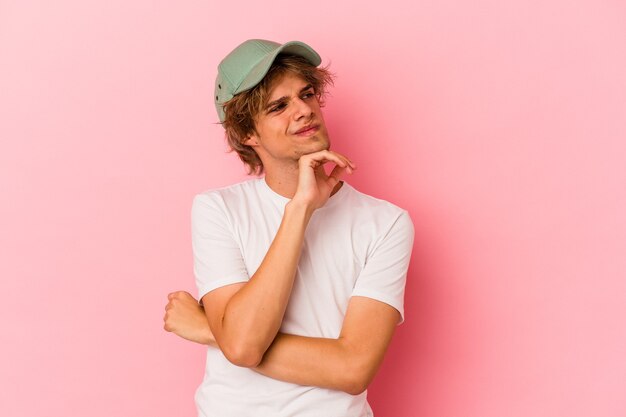 Giovane uomo caucasico con trucco isolato su sfondo rosa pensando e alzando lo sguardo, essendo riflessivo, contemplando, avendo una fantasia.