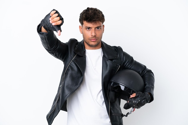 Giovane uomo caucasico con un casco da motociclista isolato su sfondo bianco che mostra il pollice verso il basso con espressione negativa