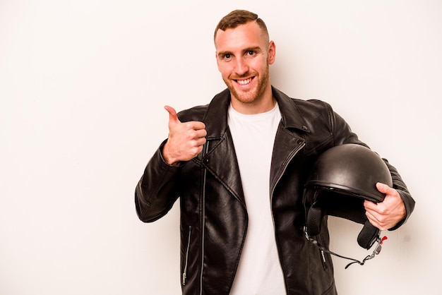 Giovane uomo caucasico con un casco da motociclista isolato su sfondo bianco sorridente e alzando il pollice