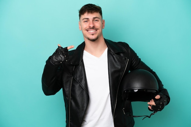 Giovane uomo caucasico con un casco da motociclista isolato su sfondo blu che dà un pollice in alto gesto