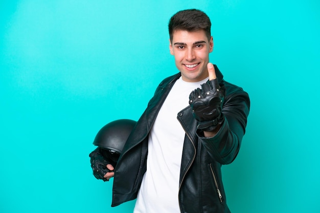 Giovane uomo caucasico con un casco da motociclista isolato su sfondo blu che fa il gesto in arrivo