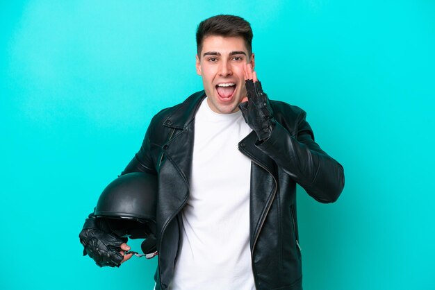 Giovane uomo caucasico con un casco da motociclista isolato su sfondo blu che grida con la bocca spalancata