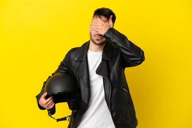 Giovane uomo caucasico con un casco da motociclista isolato su sfondo giallo che copre gli occhi con le mani. Non voglio vedere qualcosa
