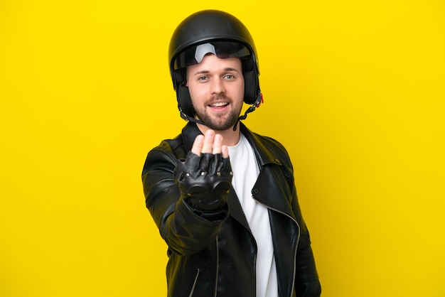 Giovane uomo caucasico con un casco da motociclista isolato su sfondo giallo che invita a venire con la mano Felice che tu sia venuto