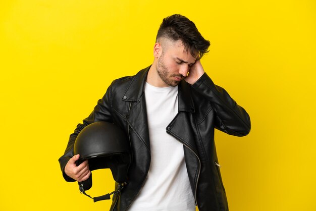 Giovane uomo caucasico con un casco da motociclista isolato su sfondo giallo con mal di testa