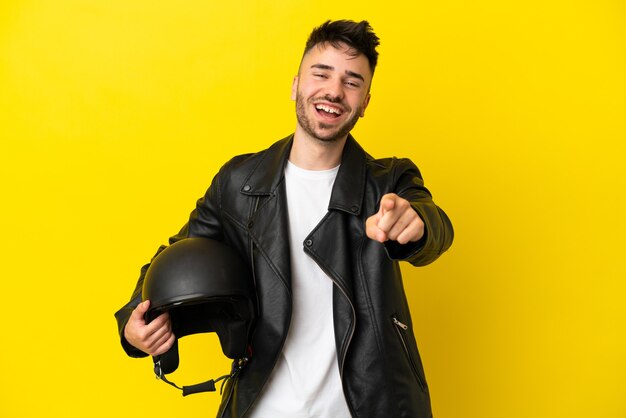 Giovane uomo caucasico con un casco da motociclista isolato su sfondo giallo sorpreso e rivolto verso la parte anteriore