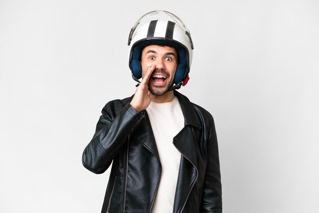 Giovane uomo caucasico con un casco da motociclista su sfondo bianco isolato con espressione facciale sorpresa e scioccata