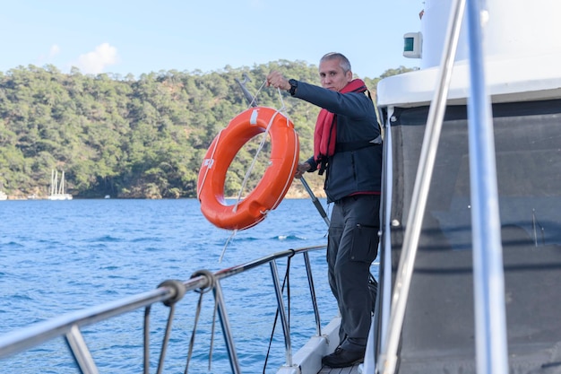 Giovane uomo caucasico con una boia di salvataggio Capitano di una barca a motore Uomo a bordo Concetto di yachting Uomo che indossa un giubbotto di salvataggio gonfiabile