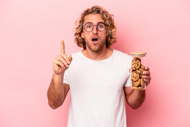 Giovane uomo caucasico con vasetto di biscotti isolato su sfondo rosa con un'idea, concetto di ispirazione.