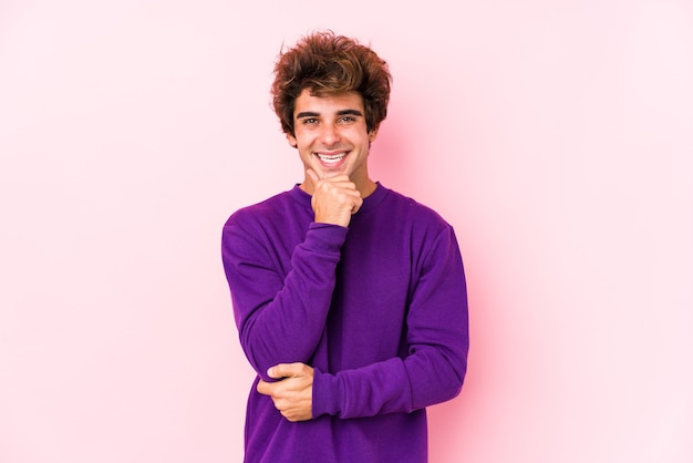 Giovane uomo caucasico contro un muro rosa isolato sorridente felice e fiducioso, toccando il mento con la mano.