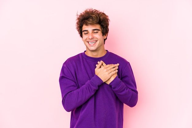 Giovane uomo caucasico contro una risata isolata rosa mantenendo le mani sul cuore, il concetto di felicità.