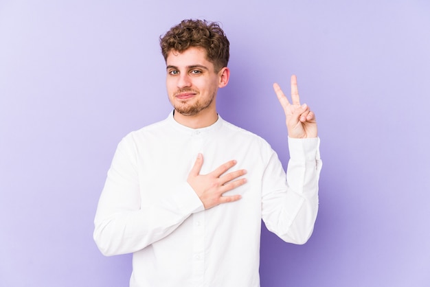 Giovane uomo caucasico dei capelli ricci biondi isolato prendendo un giuramento, mettendo la mano sul petto.