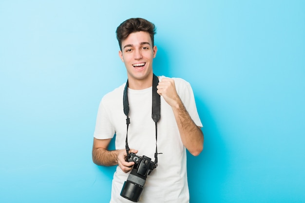 Giovane uomo caucasico del fotografo che tiene una macchina fotografica incoraggiare spensierata ed eccitata