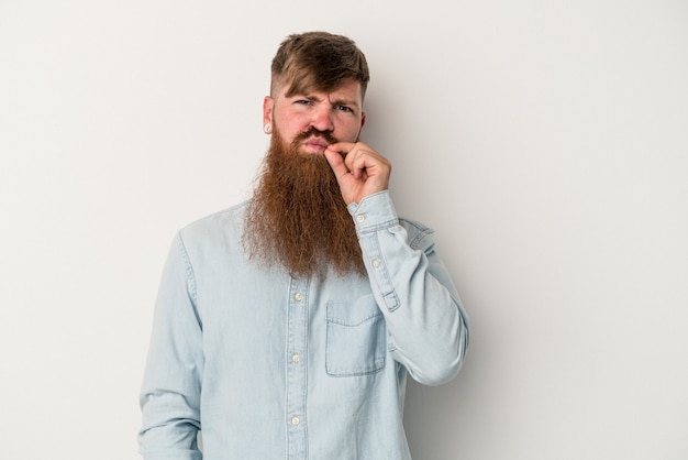 Giovane uomo caucasico dello zenzero con la barba lunga isolata su fondo bianco con le dita sulle labbra che tengono un segreto.