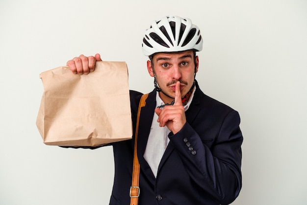 Giovane uomo caucasico di affari che indossa il casco della bici e che tiene il cibo in strada isolato su sfondo bianco mantenendo un segreto o chiedendo silenzio.