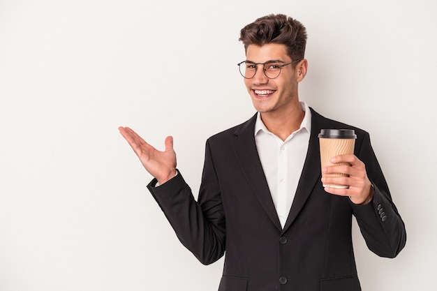 Giovane uomo caucasico di affari che tiene caffè da asporto isolato su sfondo bianco che mostra uno spazio di copia su un palmo e tenendo un'altra mano sulla vita.